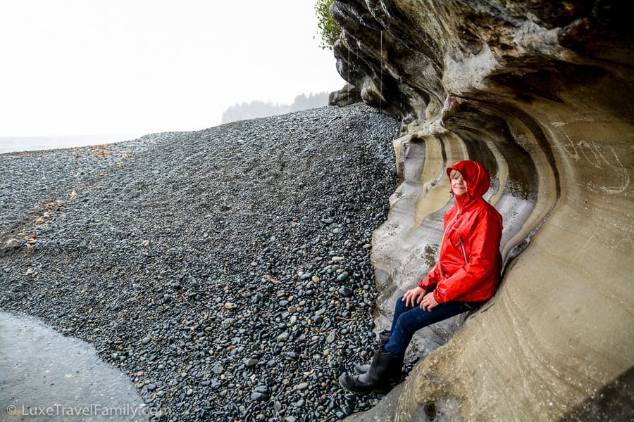 A boy sitting under a cliff near the waterfall at Sandcut Beach